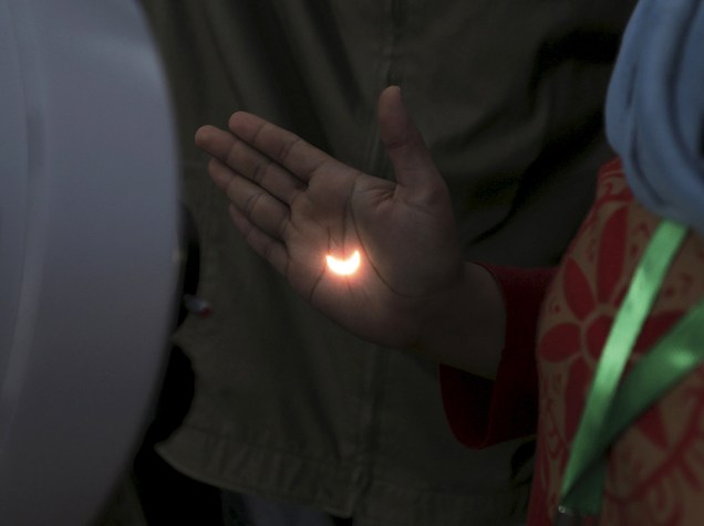 <p>Eclipse solar, que ocorreu hoje (9) na Indonésia, reflete na mão de pessoa através da lente de um telescópio</p>