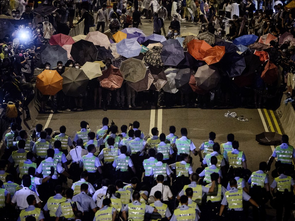 Policiais marcham em direção à manifestantes que seguram guarda-chuvas em frente ao palácio do governo, em Hong Kong
