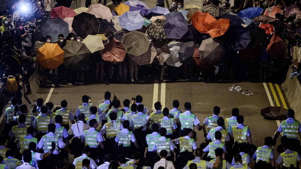 Policiais marcham em direção à manifestantes que seguram guarda-chuvas em frente ao palácio do governo, em Hong Kong