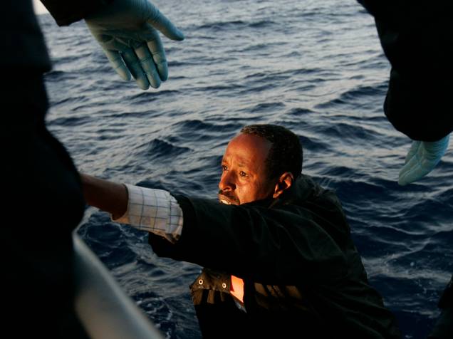 Vítima do naufrágio na costa da Líbia recebe ajuda para sair do mar. Cerca de 800 pessoas estavam a bordo quando o barco naufragou