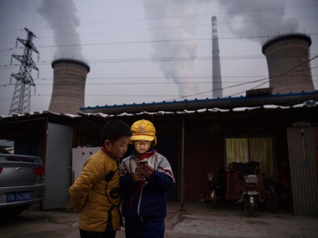 <p>Garotos chineses olham para seus celulares em próximo a uma usina em Pequim, China. Líderes de 196 países se reúnem em Paris para estabelecer metas para redução da emissão de gás carbônico em uma tentativa de criar um novo acordo global sobre as mudanças climáticas</p>