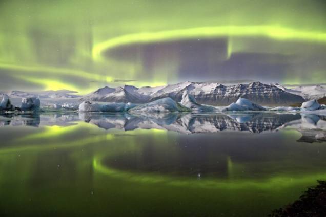 <p>Na categoria Terra e Espaço, a foto vencedora mostra uma aurora boreal refletida em uma lagoa glacial na Islândia. De acordo com James Woodend, da Grã-Bretanha, que fez o clique, esta aurora não era das mais fortes, mas o fenômeno — mesmo pouco intenso — às vezes proporciona os melhores reflexos, ainda mais com a água extremamente parada, como no caso da foto. Ao fundo está Vatnajökull, a maior massa de gelo do país. O tom esverdeado vem de átomos de oxigênio  energizados por partículas subatômicas emitidas pelo Sol, que se acumulam nos polos Norte e Sul do planeta, provocando o espetáculo fotografado</p>