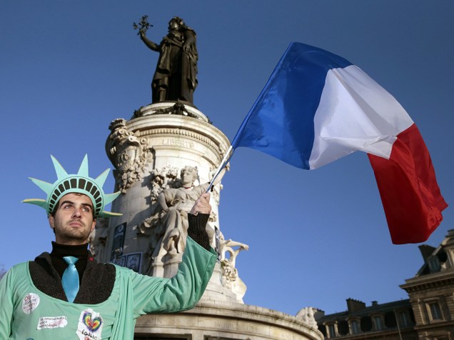 Homem vestido como a Estátua da Liberdade ergue a bandeira nacional francesa na Praça da República, em Paris, antes do início de uma grande marcha onde mais de um milhão de pessoas são esperadas além de dezenas de líderes mundiais em uma exposição histórica de desafio global contra o extremismo