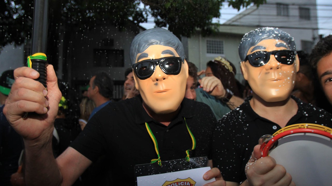 Foliões usam máscaras alusivas ao agente da Polícia Federal, Newton Ishii, que ficou famoso por escoltar réus da Operação Lava Jato, durante o desfile do Bloco Jegue Elétrico na Vila Madalena, zona oeste da capital paulista, neste sábado (06)