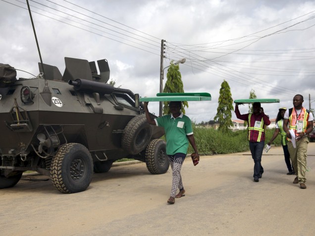 Funcionários da Comissão Eleitoral Nacional Independente passam por um veículo do exército nigeriano enquanto carregam materiais eleitorais para as cabines de votação na cidade de Otuoke - 28/03/2015