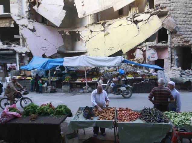 Civis compram legumes e frutas em bancas montadas em frente a edifícios danificados no bairro Bustan al-Qasr de Aleppo, na Síria - 14/10/2015
