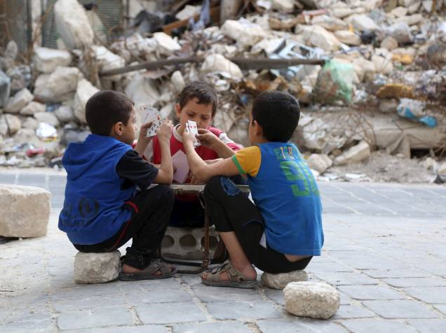 Crianças jogam cartas em meio a edifícios danificados na cidade velha de Aleppo, na Síria - 18/10/2015