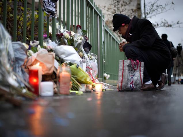 Homem se ajoelha na frente de velas e flores colocadas perto dos escritórios do jornal satírico francês Charlie Hebdo em Paris - 08/01/2015