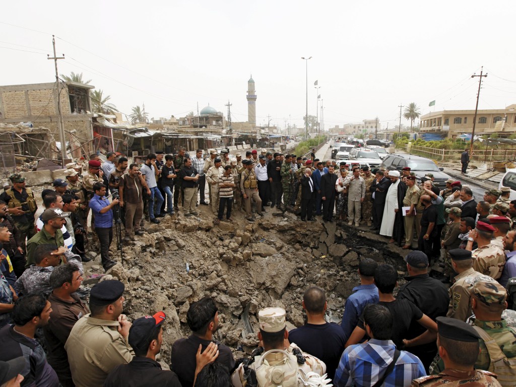 Moradores e membros das forças de segurança iraquianas se reúnem em torno do local de um ataque suicida com um carro bomba no mercado da cidade de Khan Bani Saad, a nordeste de Bagdá - 18/07/2015