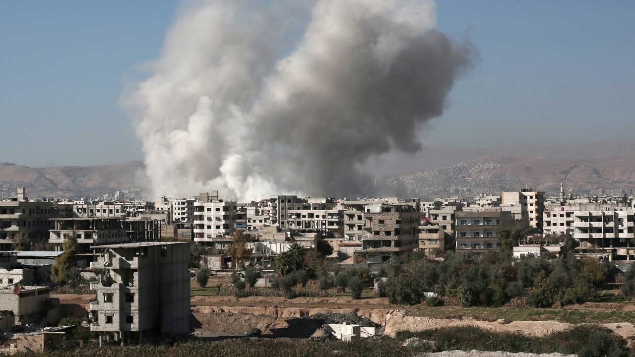 Coluna de fumaça vista sobre edifícios na sequência de um ataque aéreo no subúrbio de Damasco, controlado por rebeldes em Zamalka