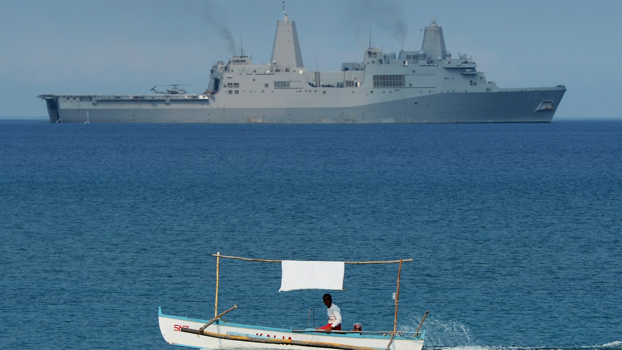 Pescador é fotografado enquanto passa pelo navio da Marinha dos Estados Unidos USS Green Bay, durante exercícios militares próximo ao recife de Scarborough, disputado entre as Filipinas e a China