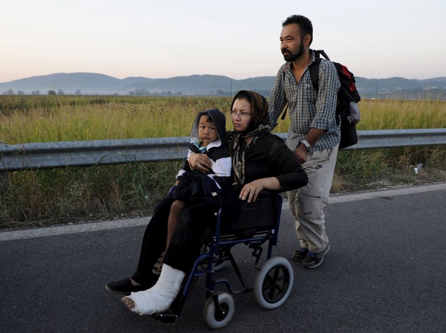 Mulher afegã com uma perna quebrada, segura seu filho enquanto seu marido empurra sua cadeira de rodas em uma estrada na da fronteira da Grécia com a Macedónia - 04/09/2015
