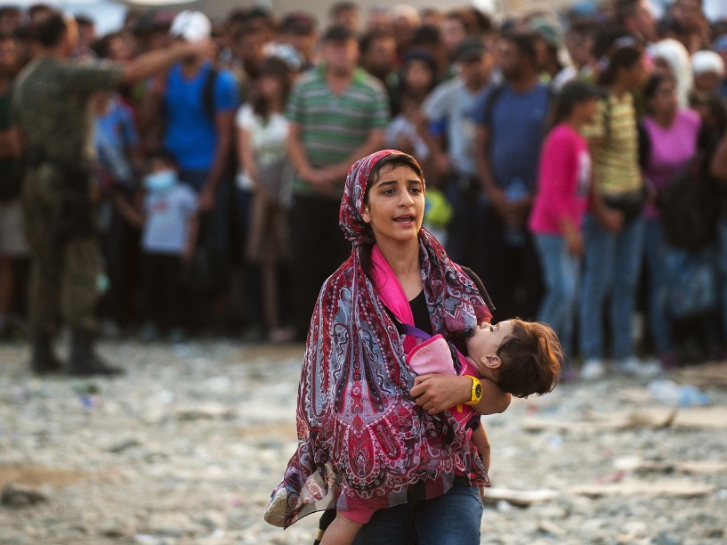 Mulher caminha com uma criança nos braços enquanto uma multidão de refugiados tenta embarcar em um trem indo para a Sérvia, na fronteira entre a Grécia e a Macedônia perto da cidade de Gevgelija - 05/09/2015