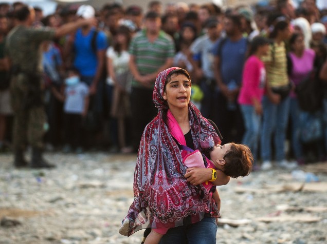 Mulher caminha com uma criança nos braços enquanto uma multidão de refugiados tenta embarcar em um trem indo para a Sérvia, na fronteira entre a Grécia e a Macedônia perto da cidade de Gevgelija - 05/09/2015