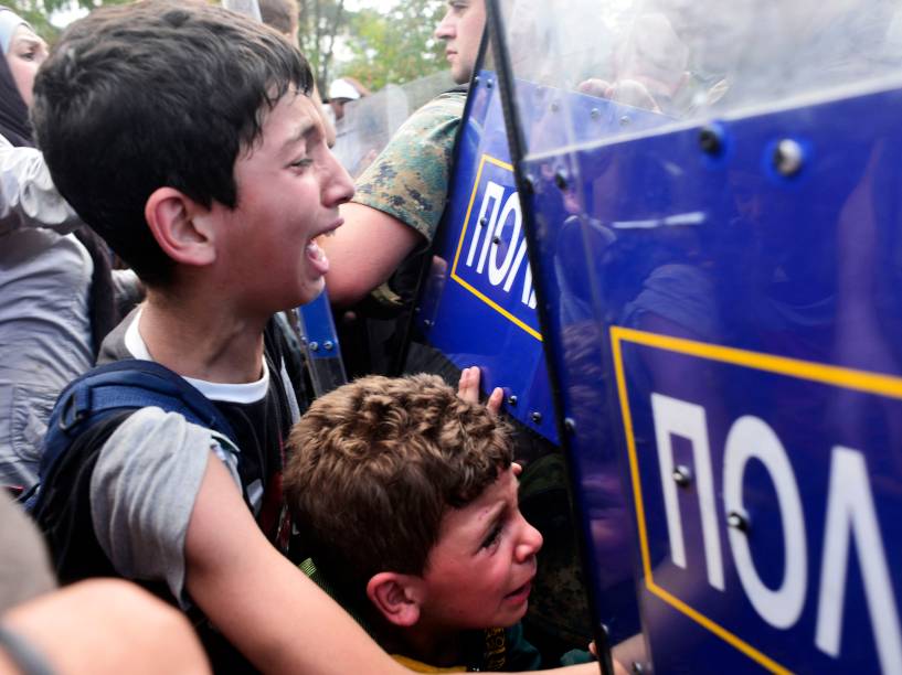 Meninos choram enquanto policiais macedônios bloqueiam um grupo de imigrantes que tentam atravessar uma área de fronteira ilegal com a Grécia - 21/08/2015