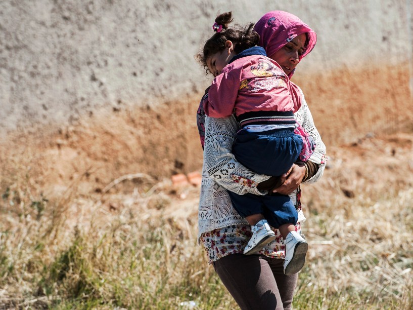 Mulher carrega uma criança enquanto se aproxima com outros imigrantes, da aldeia sérvia de Miratovac, viajando a pé desde a Macedônia - 24/08/2015