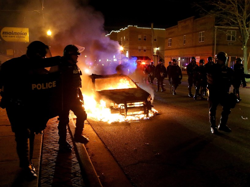Policiais passam ao lado de carro incendiado em meio a protestos em Ferguson, Missouri, pela decisão do júri de não indiciar um policial pela morte de Michael Brown, um jovem negro desarmado - 24/11/2014