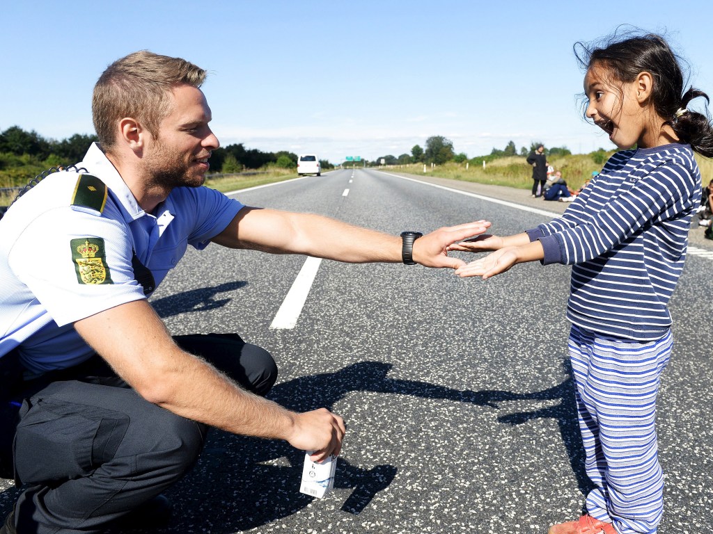 Policial brinca com uma menina refugiada em uma estrada ao norte de Padborg, na Dinamarca - 09/09/2015