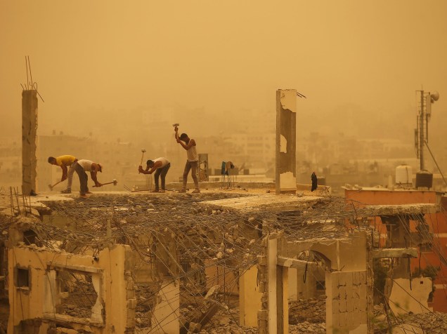 Trabalhadores palestinos removem escombros de uma casa destruída durante uma tempestade de areia em Gaza - 08/09/2015