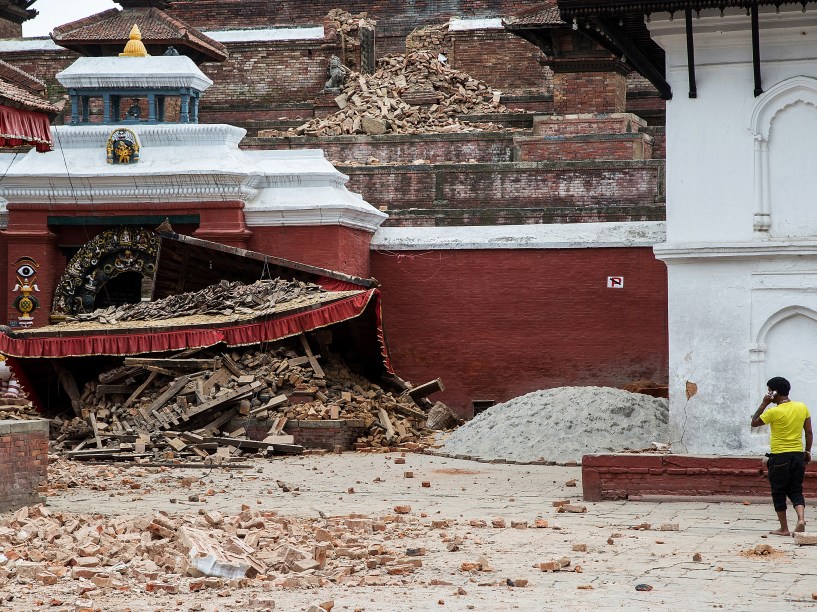Homem fala ao celular em frente a um templo que desabou após o terremoto de magnitude 7,8 no centro da cidade Katmandu, Nepal
