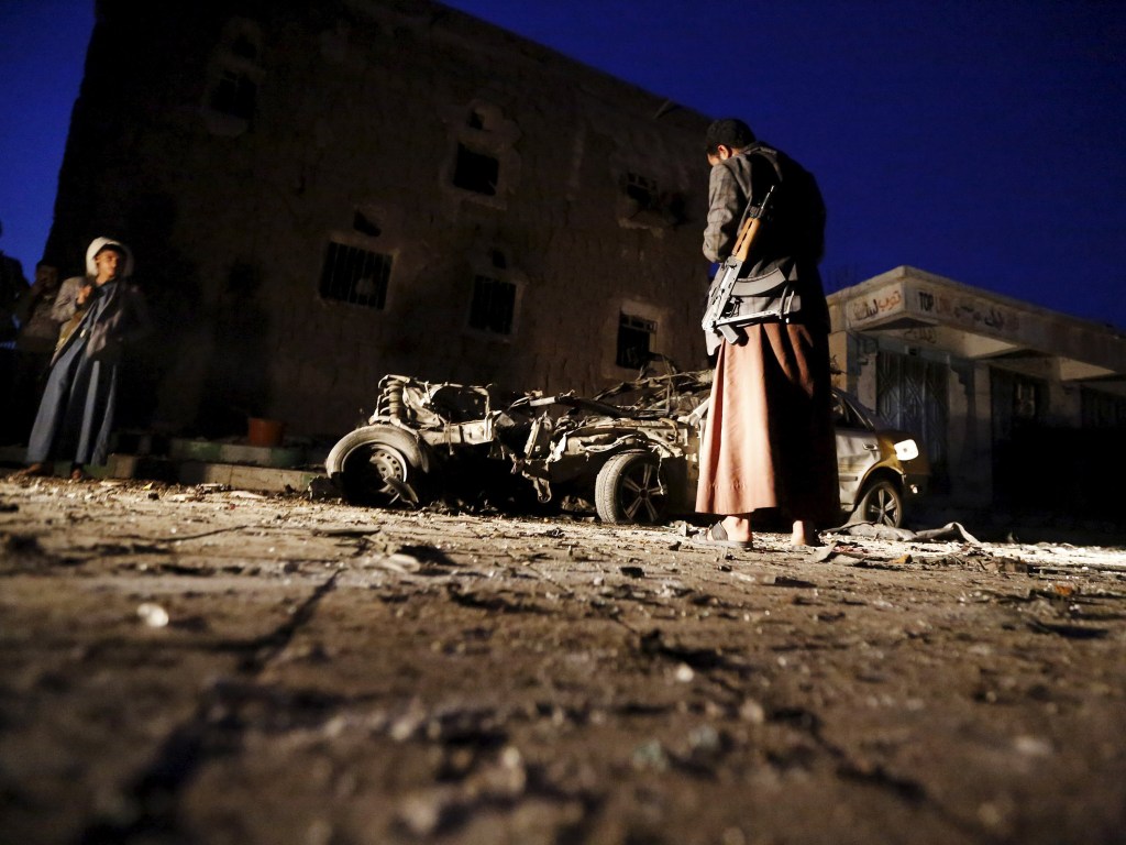 Homem armado olha para os destroços de um carro no local de um ataque com carro-bomba em Sana, capital do Iêmen. Quatro carros-bomba atingiram três mesquitas e a sede política do movimento houthi - 17/06/2015