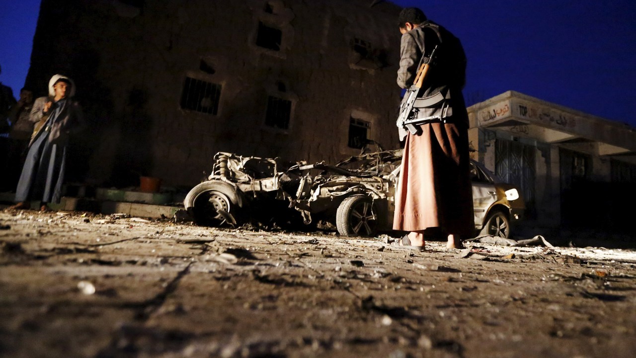 Homem armado olha para os destroços de um carro no local de um ataque com carro-bomba em Sana, capital do Iêmen. Quatro carros-bomba atingiram três mesquitas e a sede política do movimento houthi - 17/06/2015