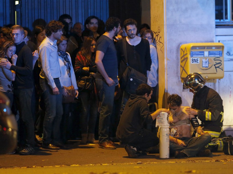 Bombeiro ajuda um homem ferido nos arredores da sala de concertos Bataclan na sequência de um tiroteio em Paris, França - 13/11/2015