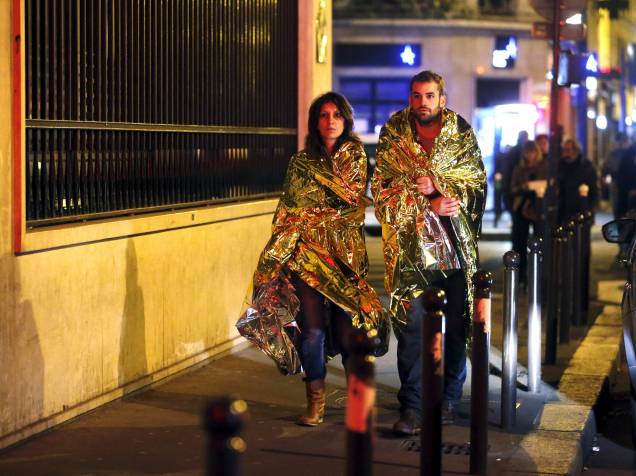 Pessoas se aquecem com cobertores térmicos enquanto andam em uma rua próxima à sala de concertos Bataclan na sequência dos ataques terroristas em Paris - 13/11/2015