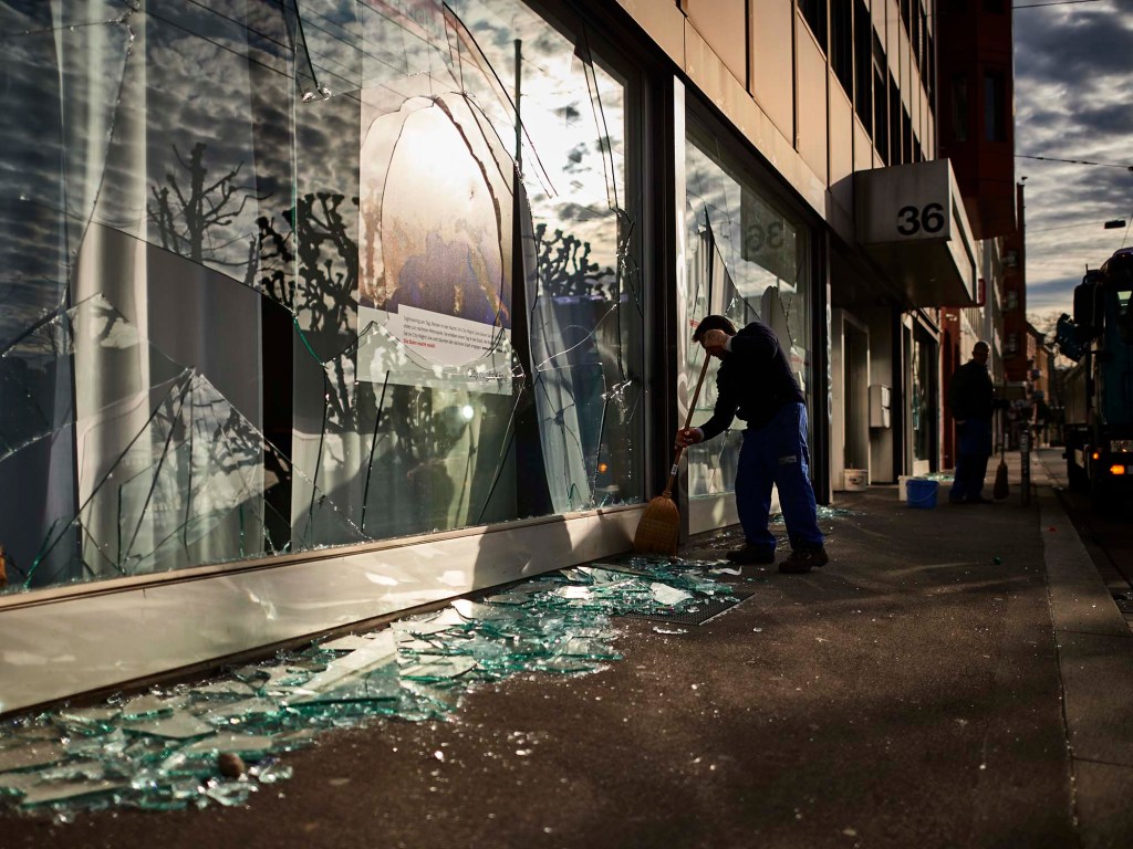 Comerciante limpa a frente de uma loja em Zurique, na Suíça, após noite violenta de protesto
