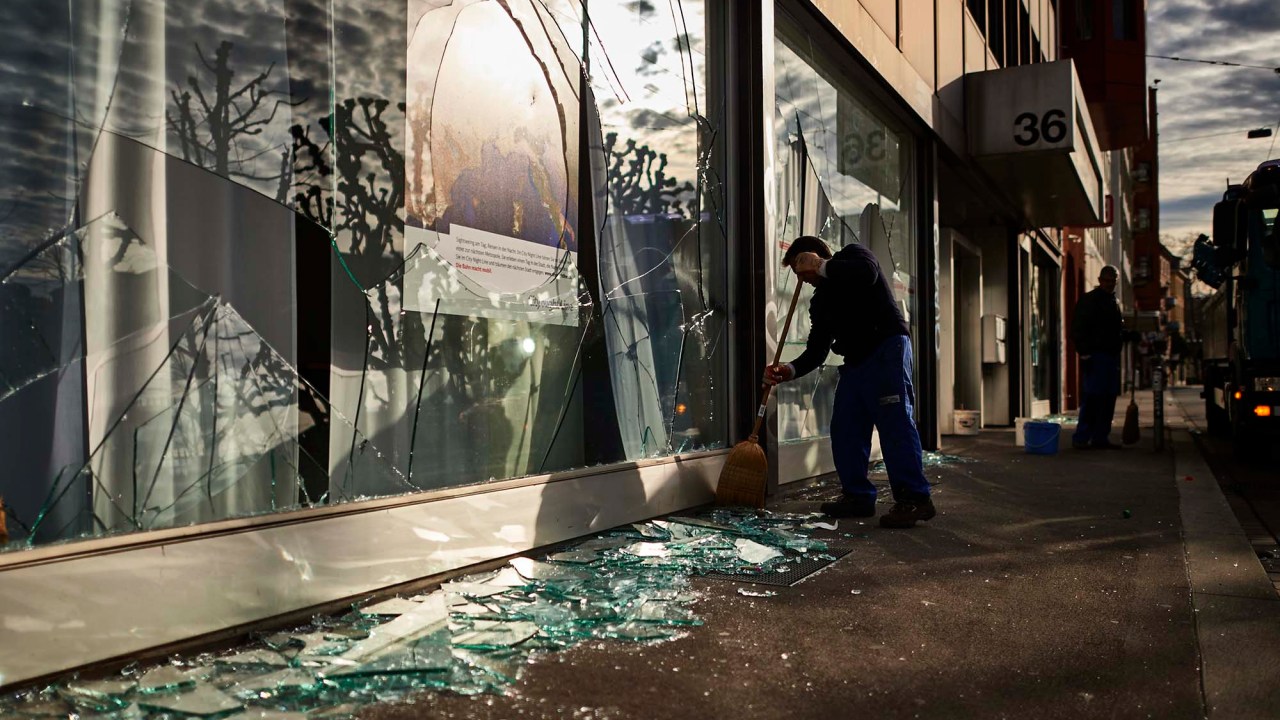 Comerciante limpa a frente de uma loja em Zurique, na Suíça, após noite violenta de protesto
