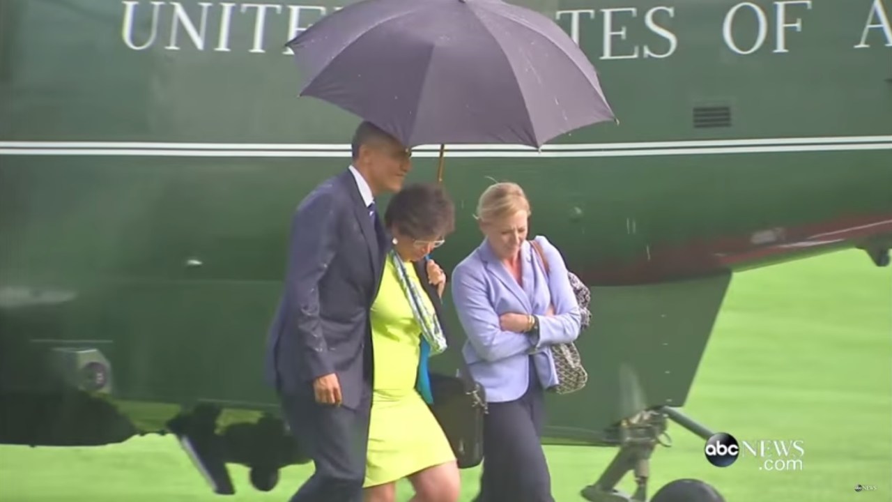 O presidente americano Barack Obama e duas funcionárias sob o mesmo guarda-chuva
