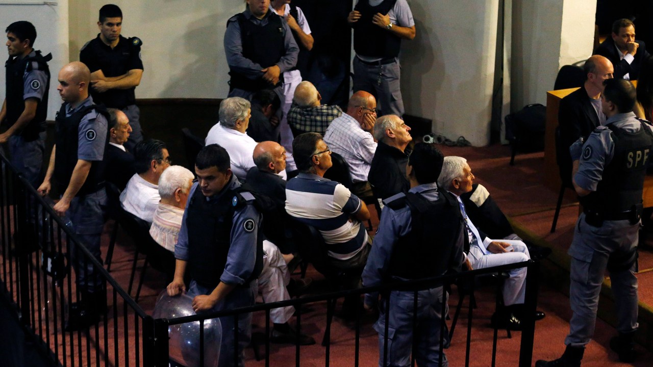 Alguns dos vinte e um homens acusados ​​de crimes contra a humanidade durante a ditadura militar da Argentina são fotografados na sala do tribunal de julgamento, na cidade de La Plata