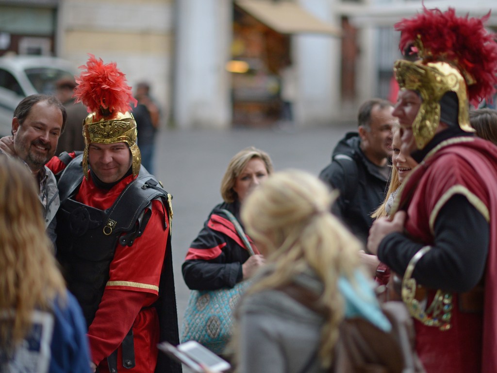 Turistas tiram fotos com homens fantasiados de soldados romanos, em Roma, Itália