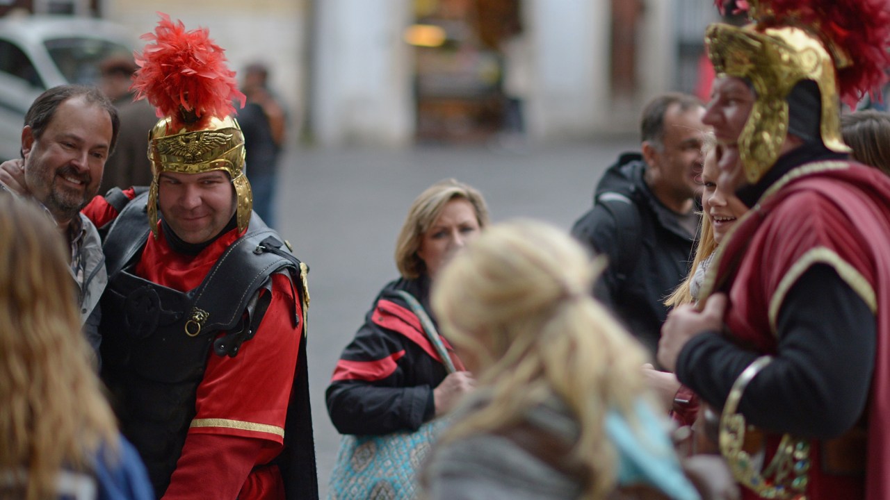 Turistas tiram fotos com homens fantasiados de soldados romanos, em Roma, Itália