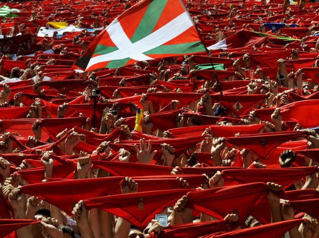 Bandeira conhecida como "Ikurrina" vista entre os tradicionais lenços vermelhos erguidos por foliões durante o Festival de São Firmino, em Pamplona, Espanha