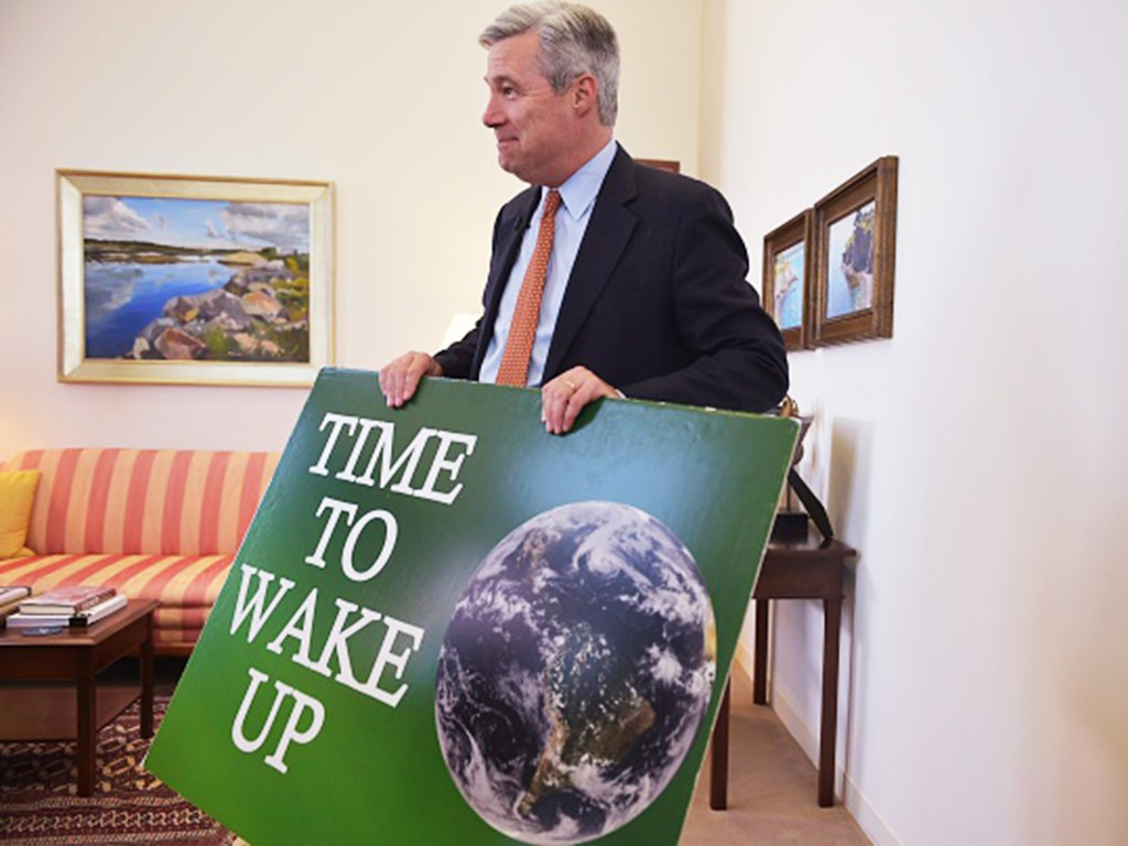 O senador Sheldon Whitehouse segura cartaz durante entrevista em seu escritório em Washington