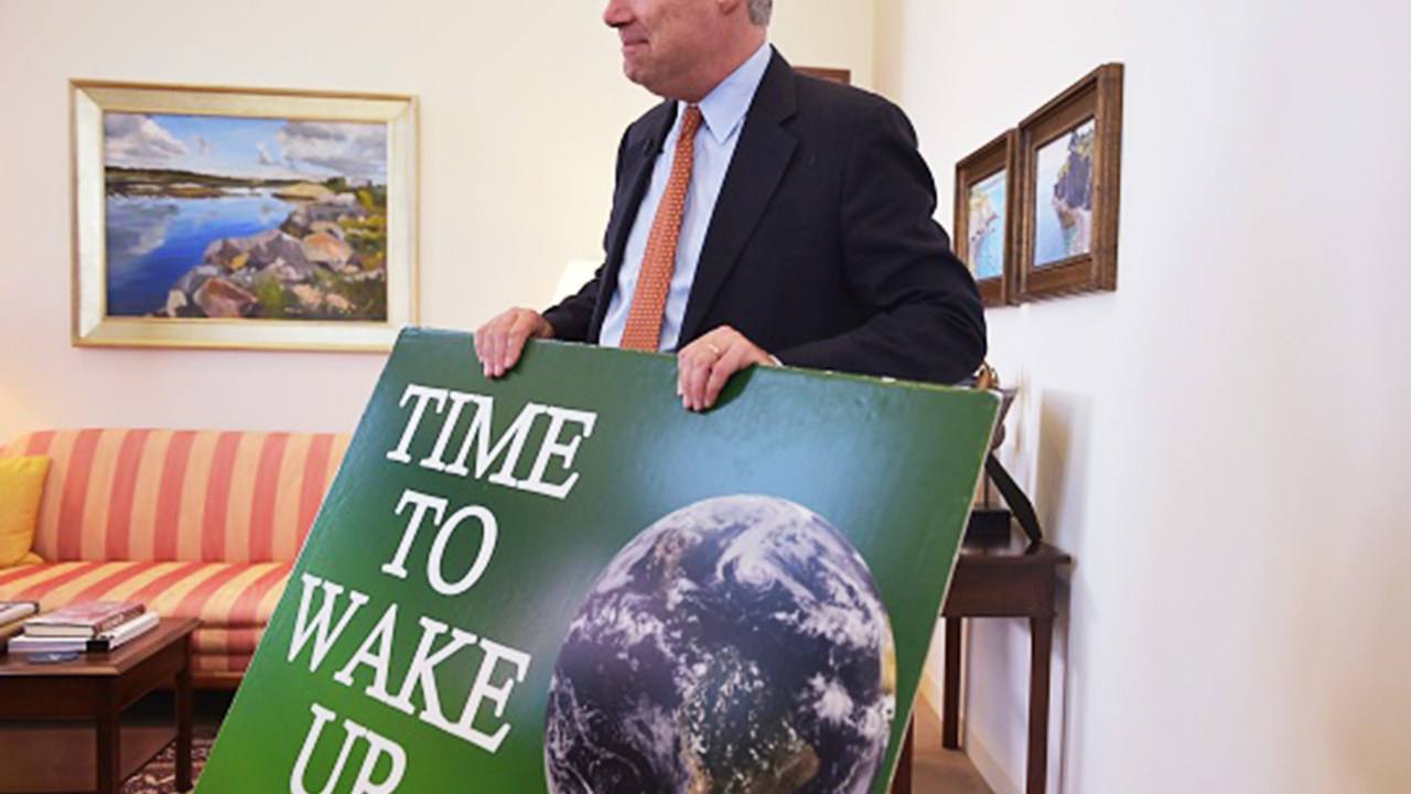 O senador Sheldon Whitehouse segura cartaz durante entrevista em seu escritório em Washington