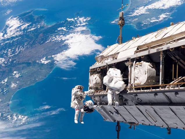 <p>Os spacewalkers Robert L. Curbeam Jr e Christer Fuglesang trabalham do lado de fora de uma estação espacial</p>