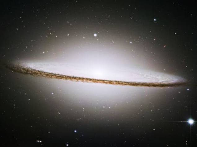<p>A Galáxia do Sombreiro é dominada por estrelas brancas brilhantes e envolvida por um disco de poeira</p>