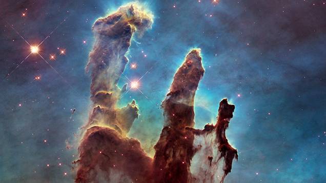 <p>As três colunas de gás se encontram na região da Nebulosa de Águia, um jovem aglomerado estelar. A foto, conhecida como Os pilares da criação, tinham uma primeira versão de 1995 e foi refeita em 2014</p>
