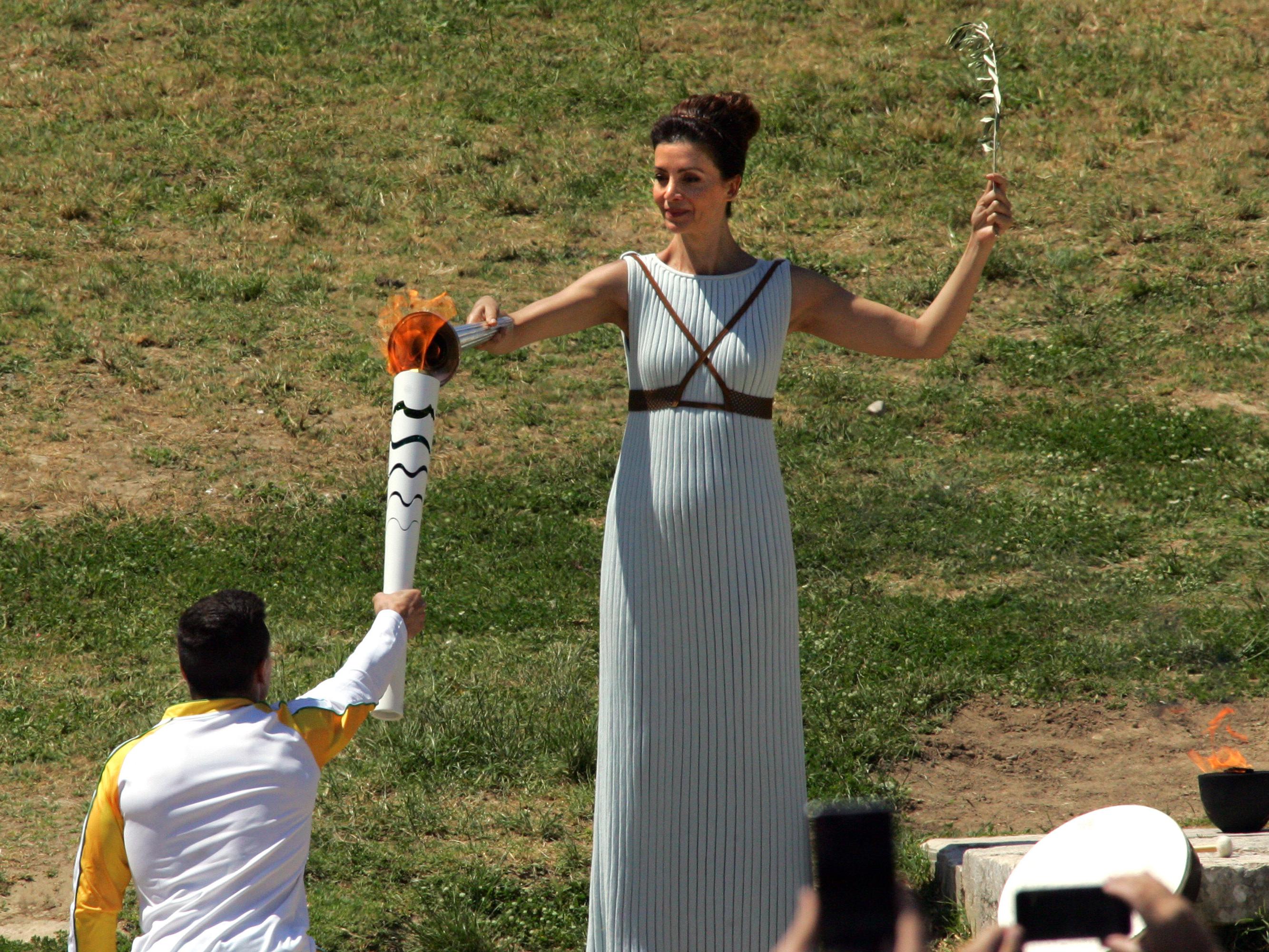 A atriz grega Katerina Lehou, no papel de sacerdotisa, passa a chama para o ginasta Eleftherios Petrounias, o primeiro a desfilar com a tocha