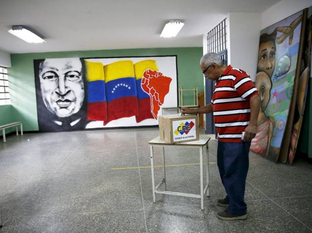 Homem deposita seu voto em frente a mural com a figura do ex-presidente Hugo Chávez em escola de Caracas, na Venezuela