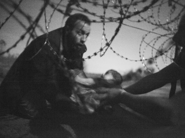 Homem passa bebê através de uma cerca, na fronteira entre Sérvia e Hungria. Foto vencedora na categoria Foto do Ano