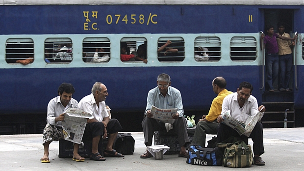 Passageiros no estado de Punjab leem jornais à espera do funcionamento dos trens