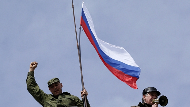 Homem com traje militar alça bandeira russa no alto da base naval da Ucrânia em Sevastopol