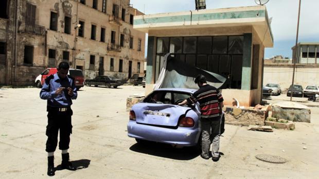 Membro da força de segurança e civil observam posto policial atacado em Bengasi, na Líbia