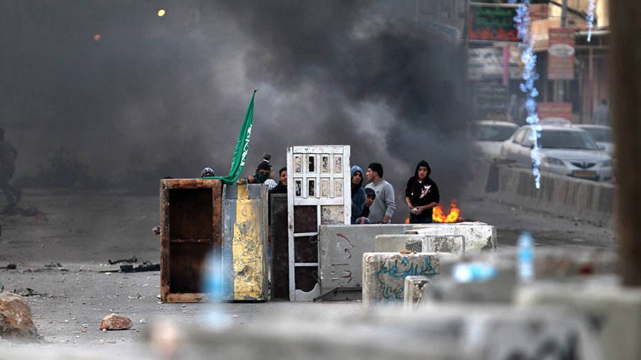 Jovens palestinos se escondem após confronto com soldados israelenses, na Cisjordânia