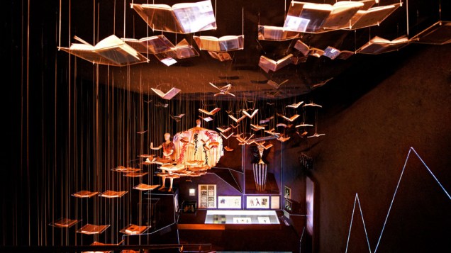 Sala com "livros voadores" destaca algumas influências de David Bowie na literatura e na moda. Ao fundo, figurinos usados na década de 1970