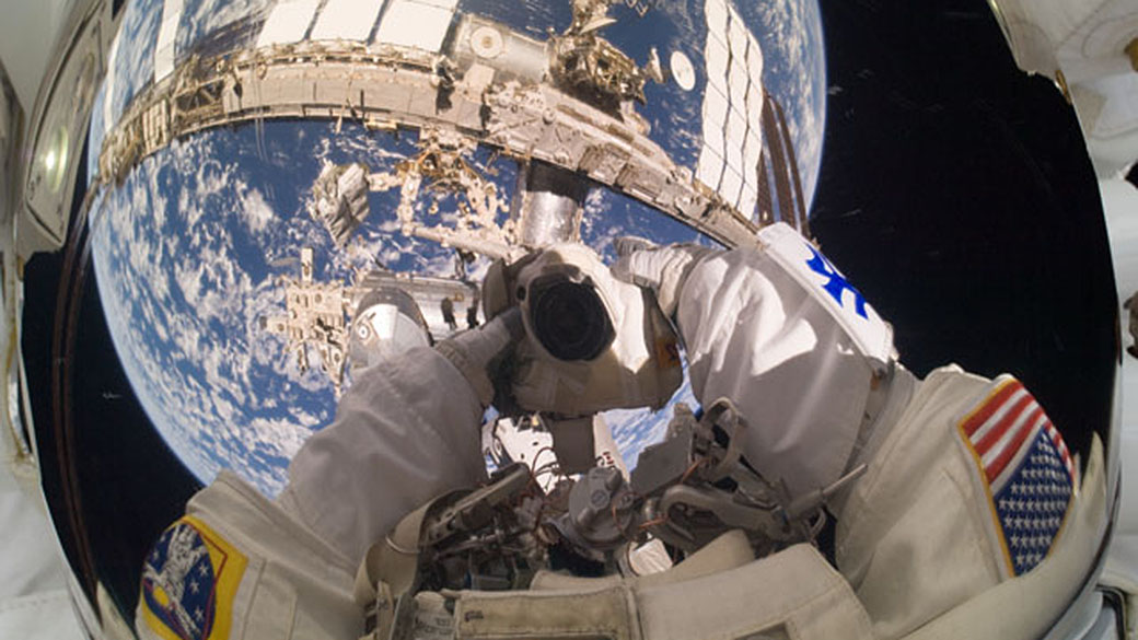 O astronauta Garret Reisman, durante uma caminhada espacial. A Terra e a Estação Espacial Internacional se refletem em seu visor