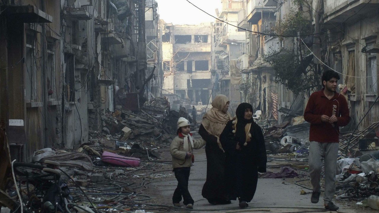 Civis caminham por um bairro destruído na cidade de Homs, na Síria